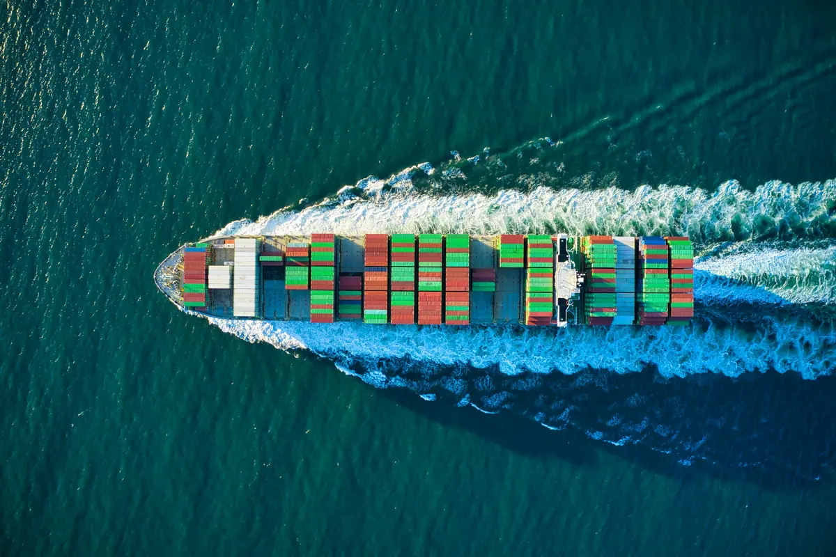 Aerial view of a loaded container ship cutting a white wake through deep blue water