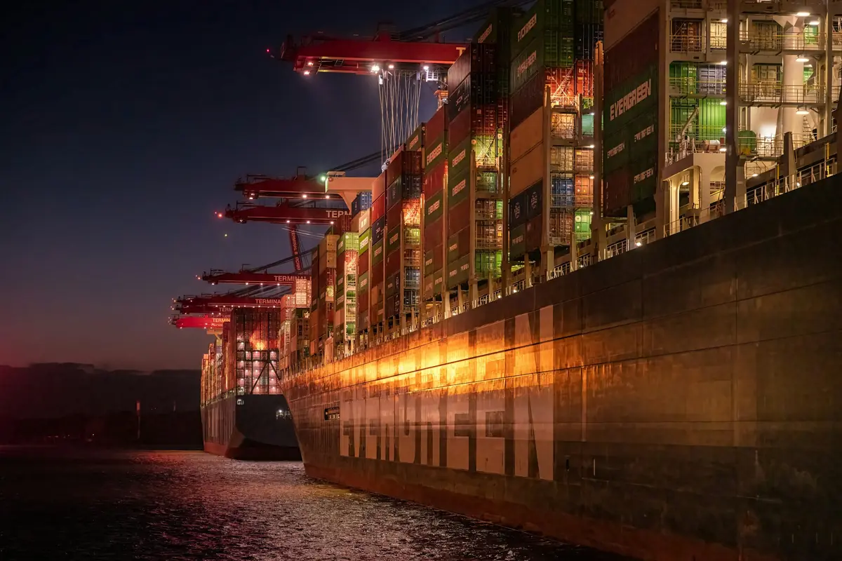Container ship hull at night alongside a lit terminal