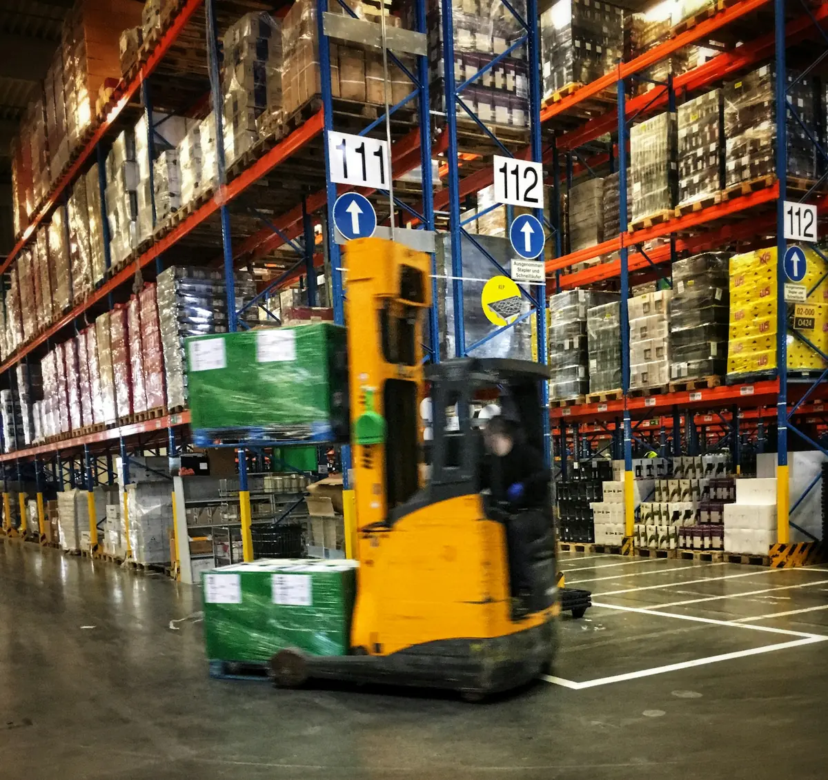 Forklift working between tall pallet racks in a warehouse